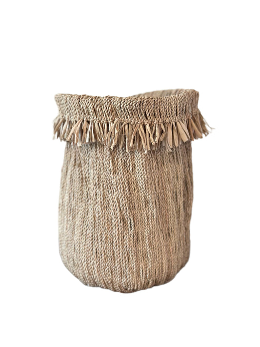 Woven basket with tassels on a wooden surface against a plain background